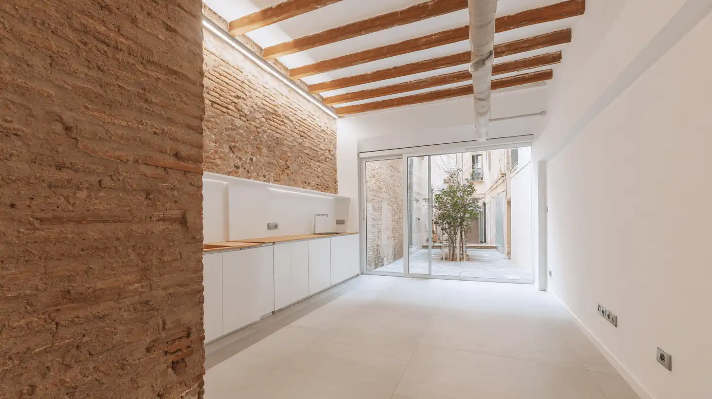 Casa de cos rehabilitada con pared de tapia, vigas de madera y cocina abierta al patio en Sabadell